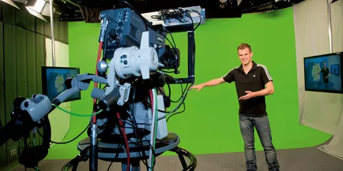 Ein Mann steht in einem Filmstudio vor einem Green-Screen und macht eine Test-Pose für die Kamera