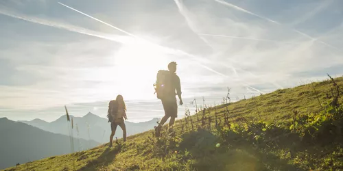 Zwei junge Menschen, die bei Sonnenschein einen Berg hochwandernd